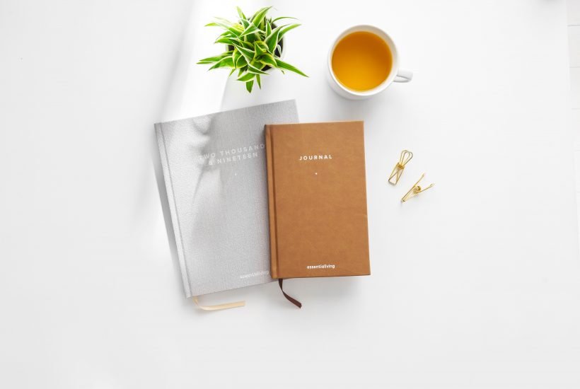 Flatlay of a plant, tea in a cup, a grey agenda with 2019 written on it and a beige journal on top of it