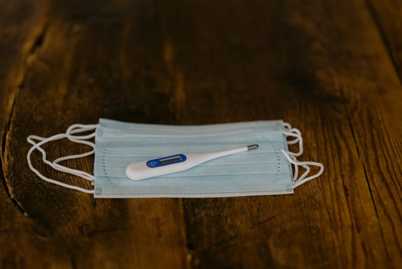 Thermometer placed on top of a face mask that's placed on a wooden surface
